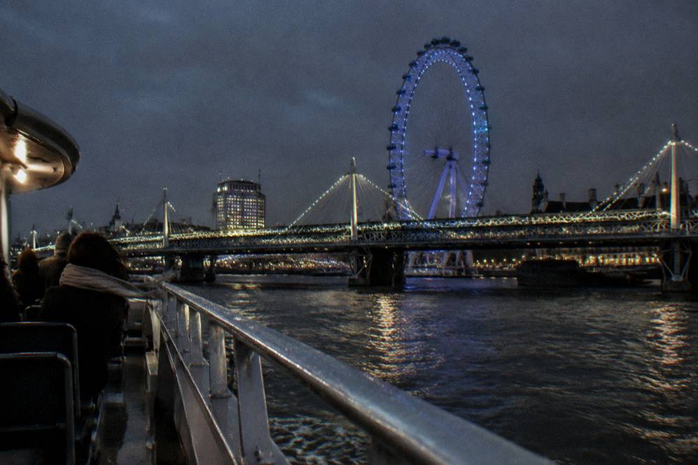 A river boat passing illuminated bridges on the Thames at night