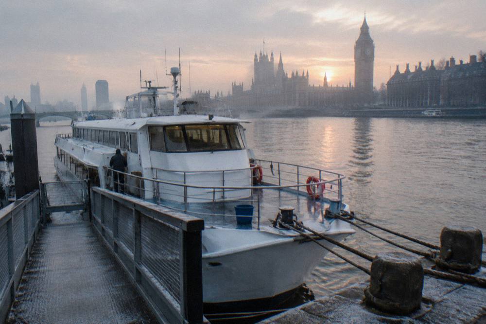 A cruise boat moored at a London pier with the city skyline behind it