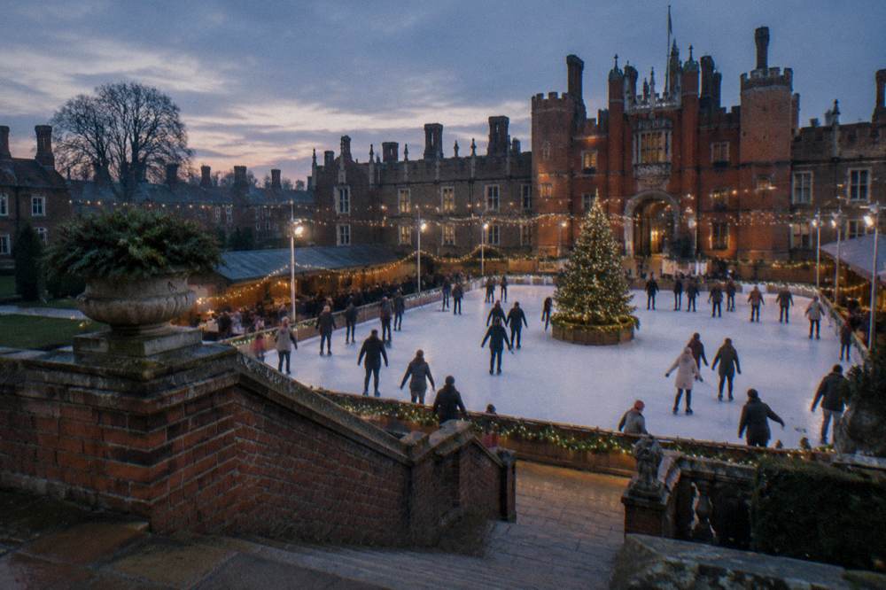 Outdoor ice rink in a floodlit courtyard with skaters circling a large lit tree
