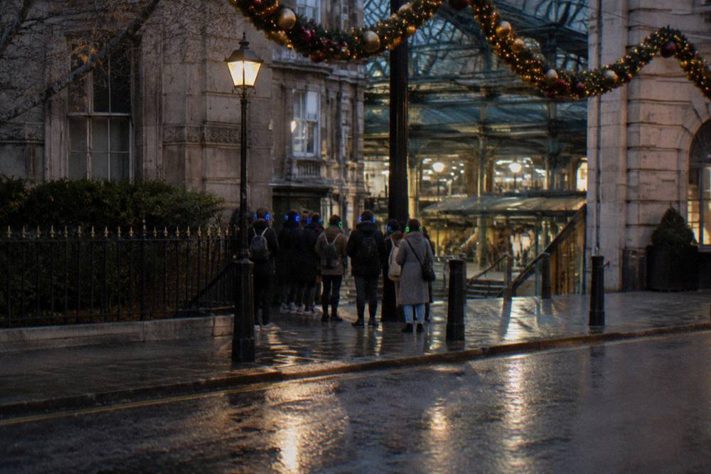 A small group of walkers on a lit London street with festive decorations overhead