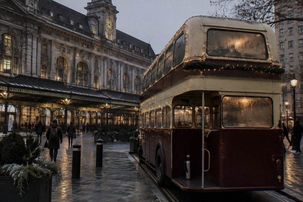 A vintage double-decker bus decorated with warm lights parked on an evening street