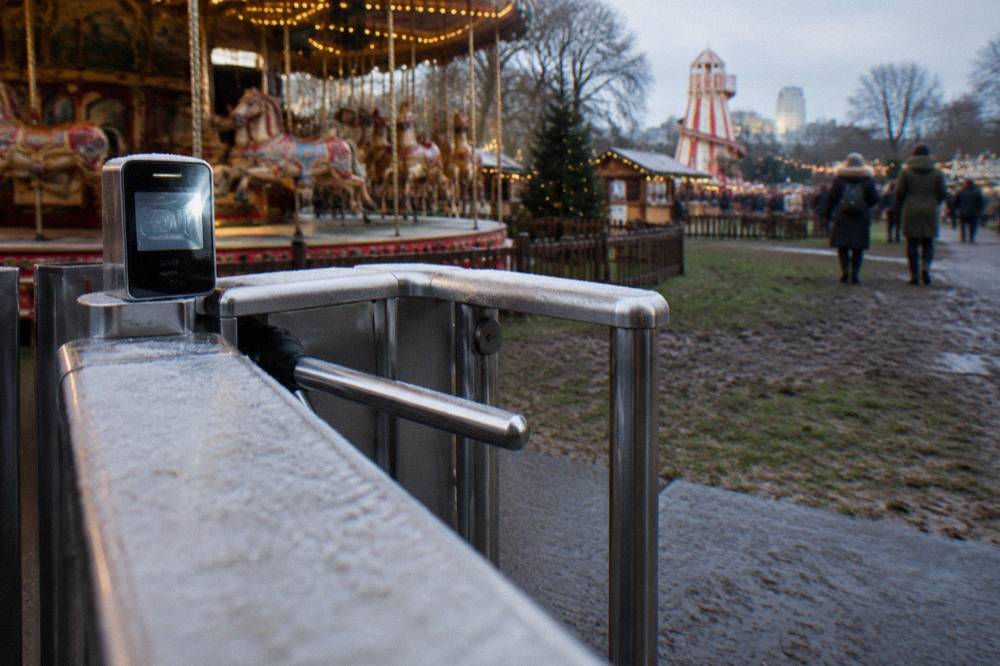 Entrance gates and ticket scanners at a fairground site with a carousel visible beyond