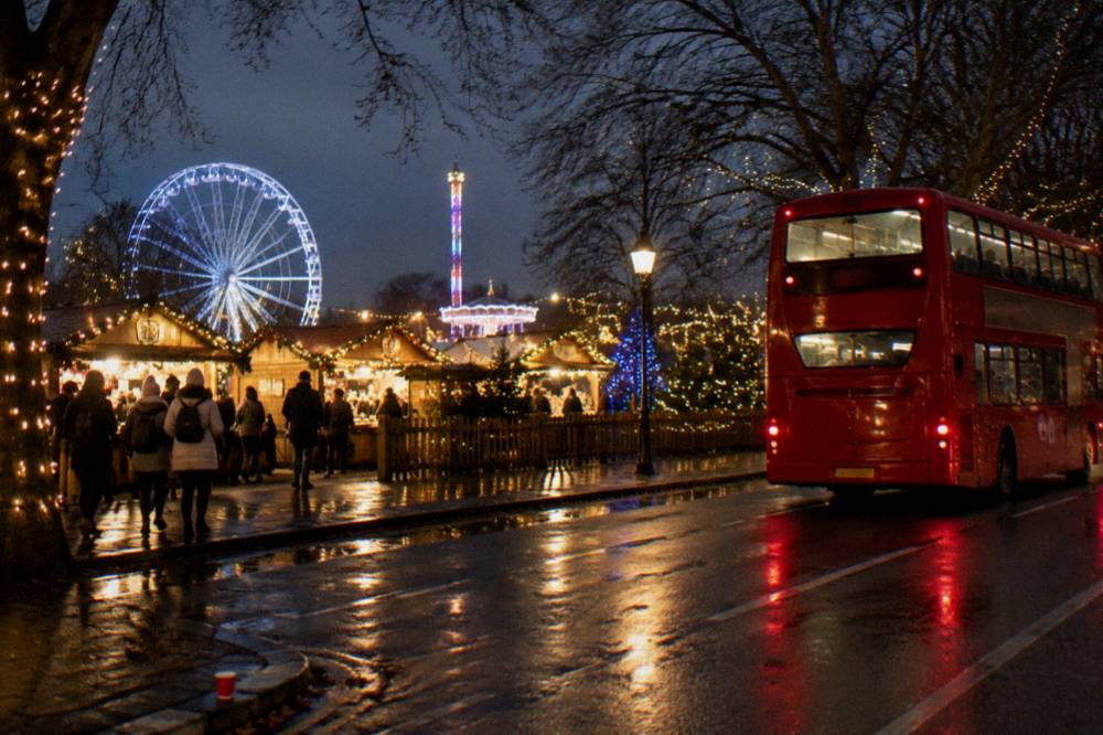 Illuminated double-decker bus passing festively decorated shop fronts on a city street at night